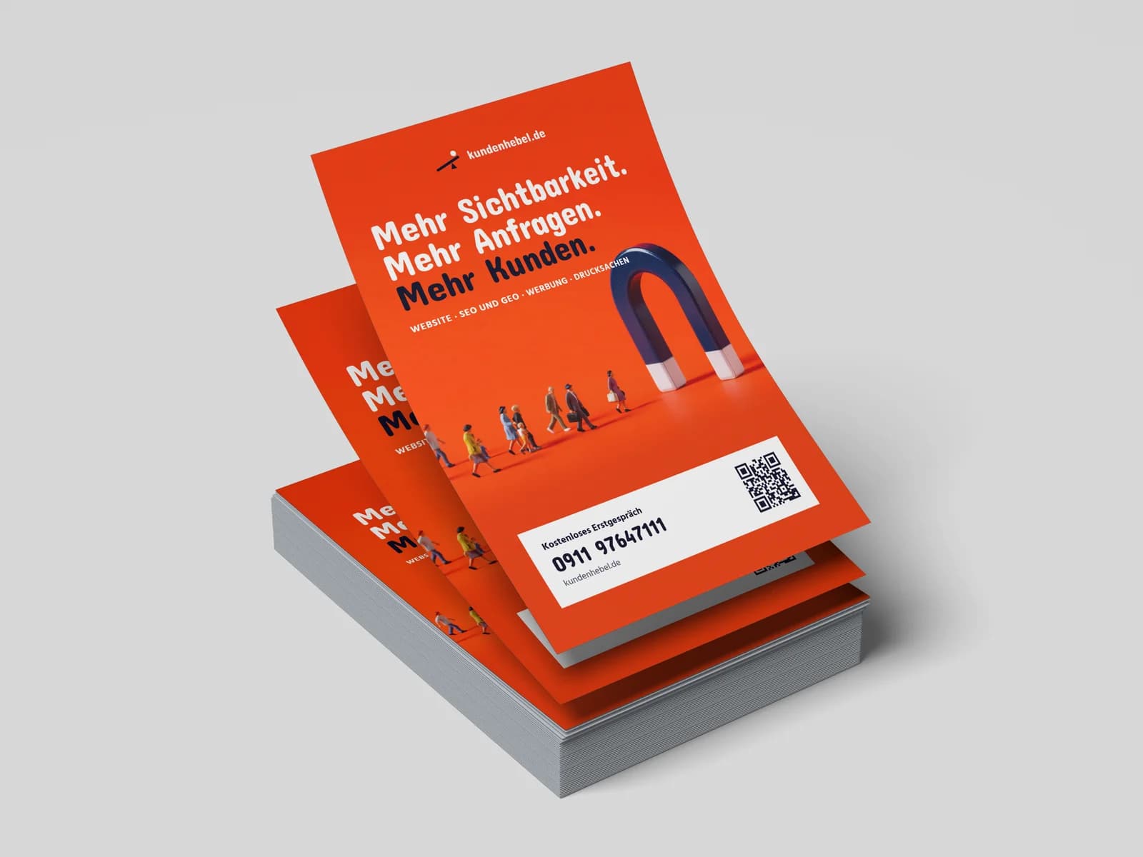 Stapel oranger A5-Flyer von kundenhebel.de: oben mittig das Logo, darunter „Mehr Sichtbarkeit. Mehr Anfragen. Mehr Kunden.“ und die Zeile „Website · SEO und GEO · Werbung · Drucksachen“, darunter Miniaturfiguren, die auf einen großen Hufeisenmagneten zulaufen, unten eine weiße Karte mit „Kostenloses Erstgespräch“, der Telefonnummer 0911 97647111 und einem QR-Code.
